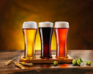Cooled glassese of different beer with condensate on the wooden table. Blurred brown background.