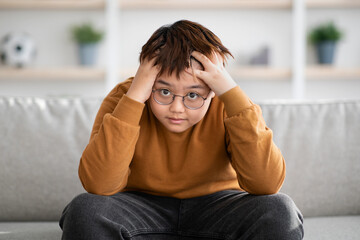 Stressed chinese boy looking at camera, home interior