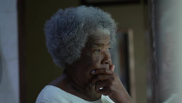 A pensive African senior woman standing by window at home a thoughtful black person in 80s