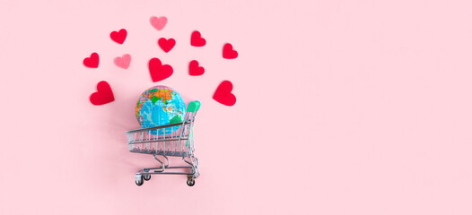 Earth Planet globe in Supermarket trolley with red hearts on pink background. Valentine's Day Sale concept. Promotion and shopping template for love and Valentine day. Top View, Flat Lay, Copy Space