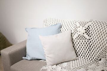 Beige couch at home with gray and blue pillow and crochet blanket, cozy sofa in apartment home. Couch decor in neutral colors interior at home.