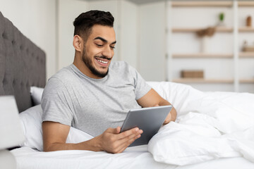 Handsome Young Middle Eastern Guy Relaxing In Bed With Digital Tablet