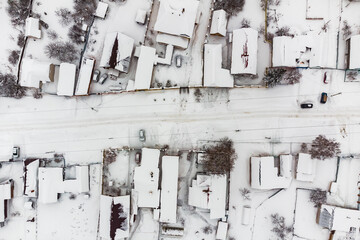 Top-down view of street with houses in snow-covered village on winter day after snowfall