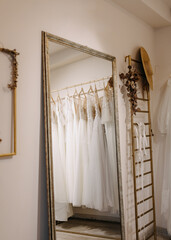 Wedding dresses hanging at an empty bridal showroom, reflected in a mirror. New collection of bohemian style wedding gowns.