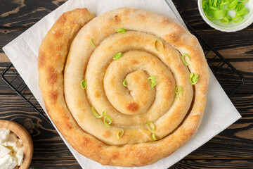 Banitsa - traditional Bulgarian spiral shape pie with brynza cheese and green onion are on brown wooden background