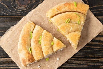 Banitsa - traditional Bulgarian spiral shape pie with brynza cheese and green onion are on brown wooden background.