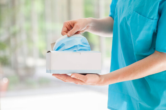 Woman Medical Professional Dressed In Blue Scrubs Pulls Safety Surgical Face Mask From Box