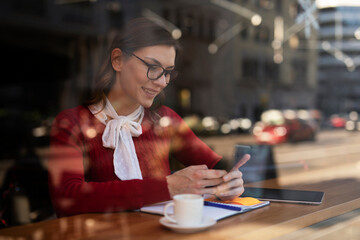 Stylish young woman drinking coffee at cafe. Beautiful girl using the phone while enjoy in fresh coffee