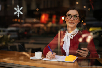 Stylish young woman drinking coffee at cafe. Beautiful girl using the phone while enjoy in fresh coffee
