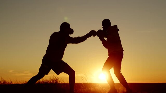 Silhouette two African-Americans man are training to boxing against background of sunset, side view. Two black men are conducting boxing sparring outdoors. Sparring concept
