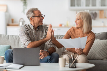Mature Couple Holding Papers And Giving High-Five Reading Bills Indoors