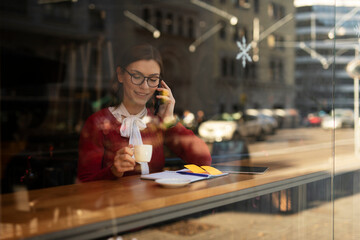 Stylish young woman drinking coffee at cafe. Beautiful girl talking to the phone while enjoy in fresh coffee