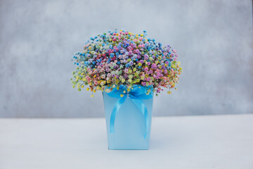 Bouquet of multi-colored gypsophila in a blue box with a bow on a gray background