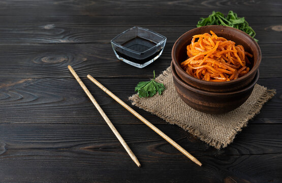 Korean seaw with spices and parsley in a clay bowl. Wooden chopsticks and soy sauce in the background. Top view, space for text