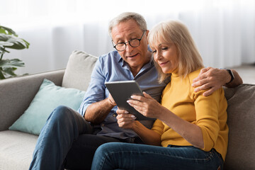Retired Couple Using Digital Tablet Computer Together Sitting At Home