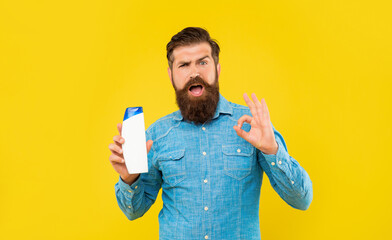 funny brutal bearded man hold shampoo bottle on yellow background, presenting toiletries. ok