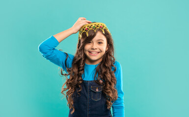 cheerful child with curly hair in queen crown on blue background, egoist