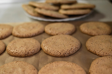 A round almond cookie that lies on a teflon sheet, against a plate of already baked cookies