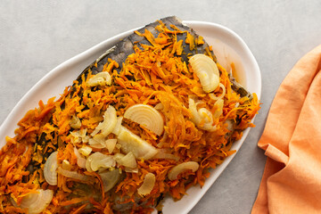Oven baked mirror carp with carrots and onions, carp on an oval dish, top view