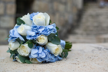 The bride's wedding bouquet is made of white roses with the addition of blue flowers, which is tied with blue ribbon, the bouquet lies on a stone slab. 