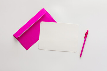 Pink envelope with blank paper and pen, greeting card or invitation mockup, top view, copy space