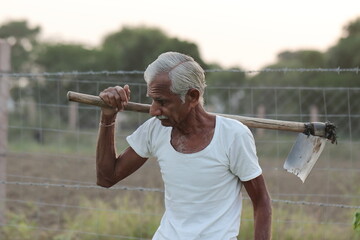 photo of An Indian senior male farmer man works in the field with a shovel on his shoulder with wearing a white vest