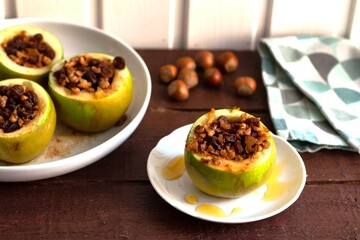 Baked green apples with nuts and raisins with honey on a white plate on a brown wooden table