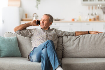 Contented Mature Man Talking On Cellphone Looking Aside At Home