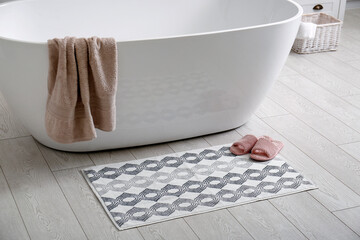 Stylish mat and slippers on floor near tub in bathroom. Interior design - obrazy, fototapety, plakaty