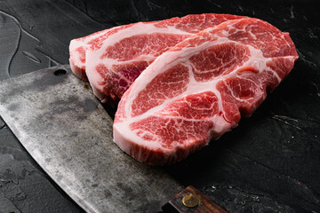 Fresh steaks from Raw pork meat, and old butcher cleaver knife, on black dark stone table background