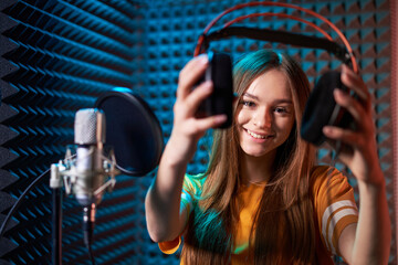 Girl in recording studio in headphones with mic over absorber panel background with closed eyes