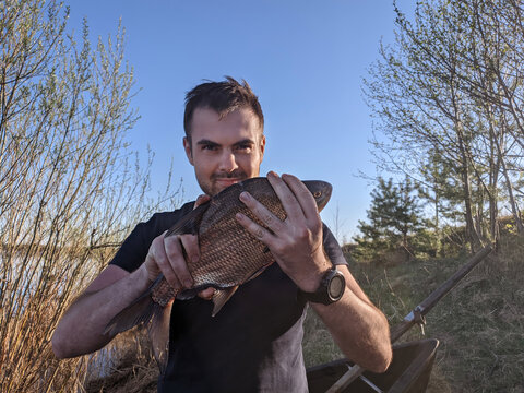 Happy amateur fisherman with vimba bream fish in hands and tackle at wild river shore