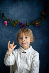 Cute little toddler boy, showing I LOVE YOU gesture in sign language on blue background, isolated image, child showing hand sings