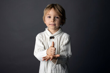 Cute little toddler boy, showing HELP gesture in sign language on gray background, isolated image,...