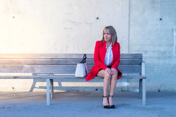 Elegant blonde woman sitting on a public park bench while looking away