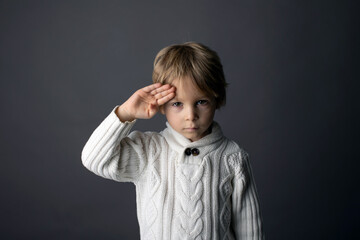 Cute little toddler boy, showing HELLO gesture in sign language on gray background, isolated image, child showing hand sings