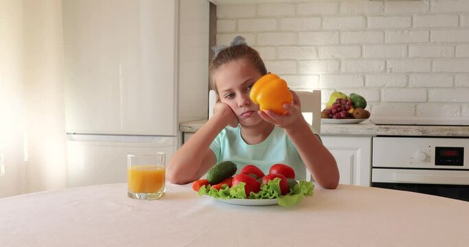 Unhappy child sitting at breakfast. Portrait of a child with vegetables in the kitchen. the child does not want to eat vegetables and fruits