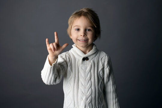 Cute little toddler boy, showing I LOVE YOU gesture in sign language on gray background, isolated image, child showing hand sings