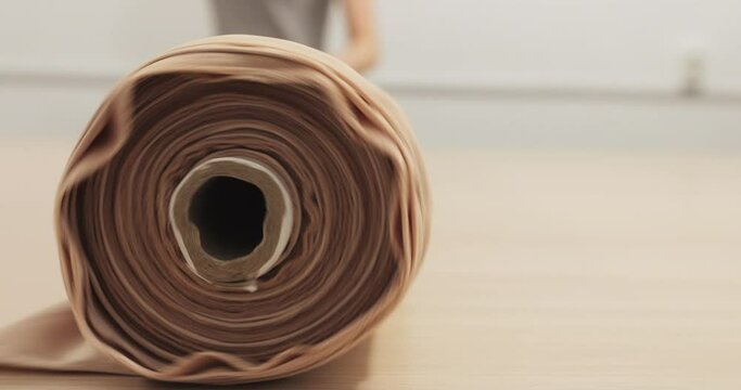 woman seamstress rolls up a roll with fabric on the table, ivory color. Rolling on the table a large pastel roll of fabric in the production of evening dresses. production of wedding dresses. macro