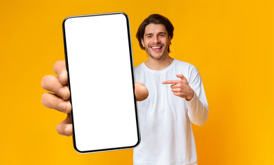 Handsome positive man showing cellphone with white blank screen and pointing on it, mockup, closeup, selective focus