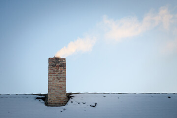 Selective blur on a smoking chimney rejecting white fume on the roof of an individual residential house covered in snow exhausting little fumes  during a cold sunny afternoon, in winter....