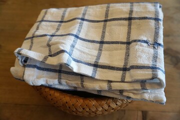 Korb aus Bast mit Stapel blau-weißer Geschirrhandtücher auf Naturholztisch 