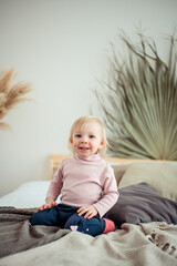 a smiling blonde girl of European appearance is sitting on the bed and looking away