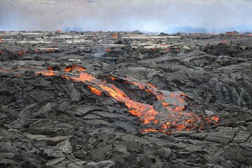 Molten lava flow at Fagradalsfjall, Iceland. Red and orange lava flows over black lava crust. Gas...