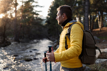 man traveler mountaineer, with backpack in the river at sunset