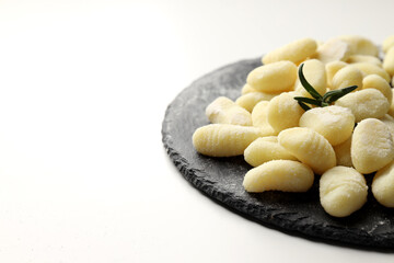 Slate board with raw potato gnocchi on white background