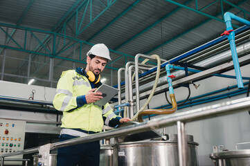Caucasian technician engineer man in uniform with tablet checking and control boiler tanks and liquid pipeline in production line at factory