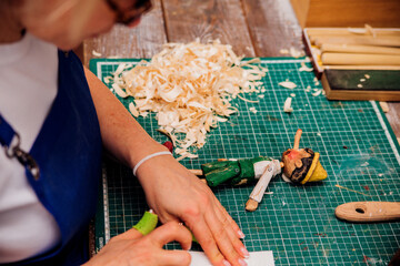 A wooden toy in women's hands. A female carpenter cuts wood with a knife in a carpentry or...