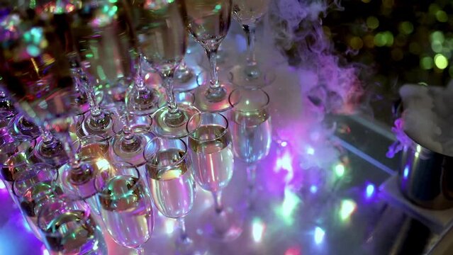 Pyramid of champagne glasses. The tower is undercut by bright lights. Full glasses of sparkling wine at a restaurant party. Holiday, wedding, birthday, event. Dry ice. Champagne with smoke
