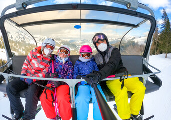 Family riding ski lift cable car on winter vacation skiing wearing masks.
